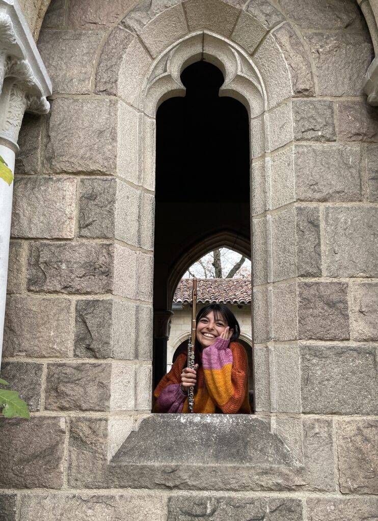 Anjali Shinde with her flute at the Met Cloisters. She is posing in a cathedral-like window.